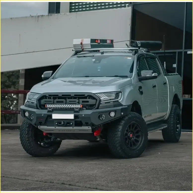Silver ford ranger with black off-road tires and rugged front bumper featuring rockarmor gt hoopless bullbar and sliders