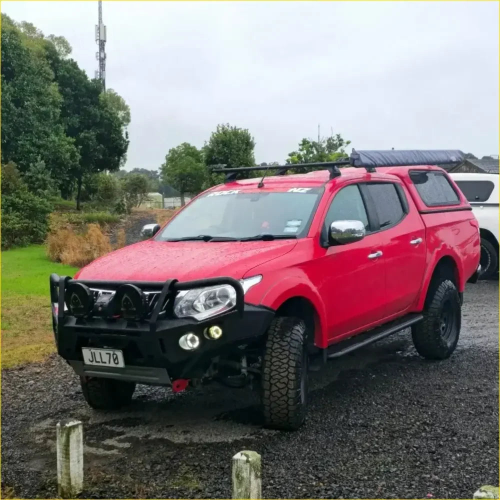 Red mitsubishi triton pickup with black roof rack and front bumper featuring gt hoop bullbar and rock sliders